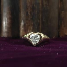 a heart shaped diamond ring sitting on top of a purple velvet covered surface with wood behind it