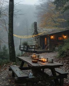 a picnic table with candles on it in front of a log cabin surrounded by trees