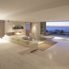 a living room filled with furniture and a large window overlooking the ocean at night time