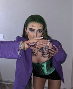 a woman with green hair and makeup wearing a purple jacket is posing for the camera