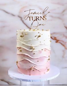 a pink and white cake with gold sprinkles sits on a marble table