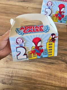 two boxes with spiderman stickers on them sitting on a wooden table next to each other