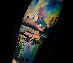 a man's arm with a colorful mountain and lake tattoo on the left forearm