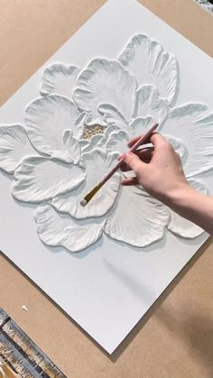 a person is painting a flower on a piece of white paper with a brush in their hand