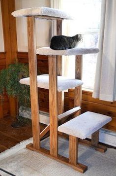 a cat sitting on top of a tall wooden scratching tower in front of a window