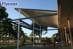 an awning on the side of a building with picnic tables under it and trees in the background