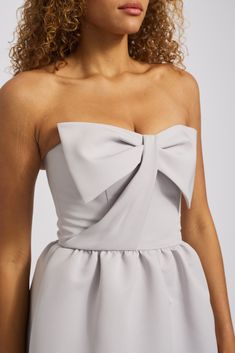 a woman with curly hair wearing a grey strapless dress and holding her hands in her pockets