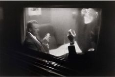 black and white photograph of man sitting in front of television with woman standing next to him