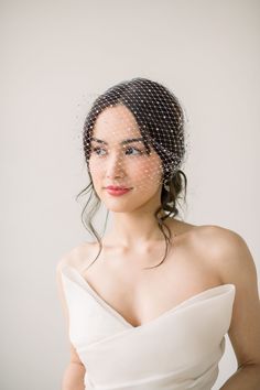 a woman in a white dress wearing a birdcage veil on her head and shoulder