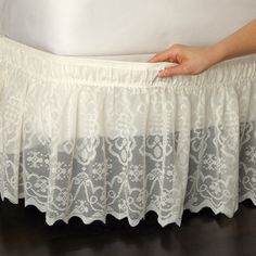 a woman's hand is holding the edge of a bed skirt with white lace on it