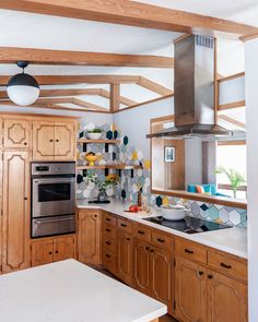 a kitchen with wooden cabinets and white counter tops, stainless steel oven hood over the stove