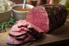 a sliced up roast beef sitting on top of a wooden cutting board next to mashed potatoes