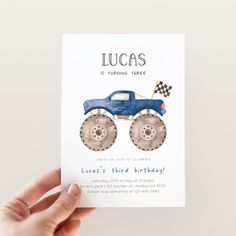 a hand holding up a birthday card with a monster truck on it and the words lucas is turning three