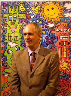 a man wearing a suit and tie standing in front of a wall with colorful paintings