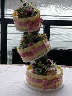 three tiered cake with flowers and ribbons sitting on top of a white table cloth