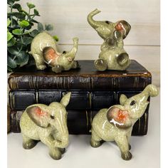 three ceramic elephants sitting on top of an old book next to a potted plant