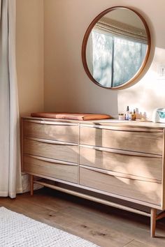 a dresser with a round mirror above it in a room that has wood floors and white walls