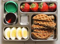 a lunch box with eggs, strawberries and waffles