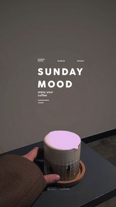 a person holding a cup on top of a black table with the words sunday mood above it