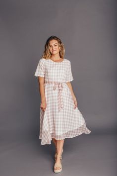 The Clemmie Plaid dress has a beautiful pink plaid pattern. It features a zipper in the back and a tie around the waist. Perfect for all your summer activities. Model is 5’5″ and wearing a Small 100% Polyester  Small: Bust  36″ Length  43″ Medium: Bust  38″ Length  44″ Large: Bust  40″ Length  45″ Spring Beach Plaid Dress, Short Sleeve Pink Dress With Tie Back, Pink Short Sleeve Dress With Tie Back, Gingham Midi Length Dress For Daywear, Gingham Midi Dress For Daywear, Pink Short Sleeve Dress For Picnic, Casual Pink Plaid Dress With Short Sleeves, Plaid Midi Sundress, Plaid Midi Length Sundress