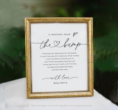 a sign that is sitting on top of a white table with a gold framed frame