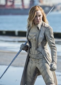 a woman dressed as star trek cosplay walking on the beach with a stick