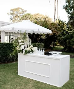 an outdoor bar with white flowers and wine glasses on the counter under an umbrella in front of a house