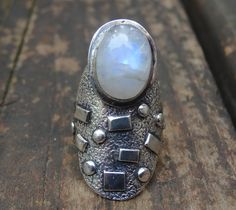 💙Handmade, Natural Rainbow Moonstone Sterling Silver Statement Ring Size 7 💙Featured in this listing is a sterling silver, handmade, natural stone ring. This lovely ring features a beautiful, Natural Rainbow Moonstone oval 14x11mm glowing stone. The stone has been bezel set into a handcrafted, unique setting made with all Sterling Silver. Detailed texturing, and rectangular and round accents, with oxidization, and a thick 8mm band. All details have been hand made. Gemstone: Natural Rainbow Moo Handmade Celestial Moonstone Ring In Moon Shape, Silver Moonstone Ring Stamped 925, Unique Silver Moonstone Ring In Sterling Silver, Handmade Silver Moonstone Ring, Silver Moonstone Ring With Stone Setting, Handmade Silver Moonstone Ring For Spiritual Purposes, Unique Silver Cabochon Moonstone Ring, Unique Silver Moonstone Ring With Stone Setting, Unique Silver Moonstone Ring With Cabochon