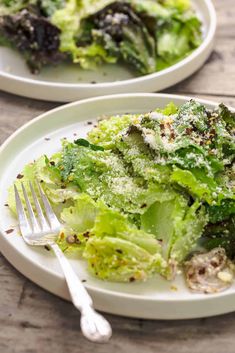 two white plates topped with lettuce covered in seasoning