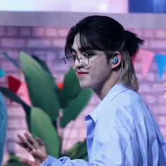 a woman with glasses is standing in front of a brick wall and cactus plant wearing ear buds