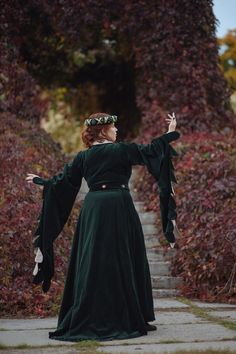 a woman in a green dress standing on a path with her arms spread wide open