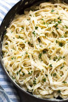 a skillet filled with pasta and parsley on top of a blue checkered table cloth