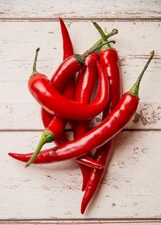 three red hot peppers sitting on top of a white wooden table next to each other