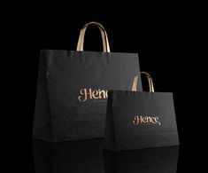 two black shopping bags with gold lettering on the front and back, sitting side by side