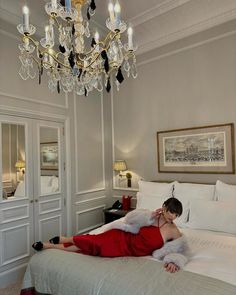 a woman laying on top of a bed in a bedroom next to a chandelier