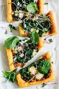 four pieces of bread with spinach and cheese on top, sitting on wax paper