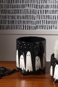 two black and white halloween planters with ghost faces painted on them, sitting on a wooden table