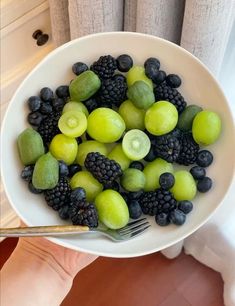 a white bowl filled with green and black fruit next to a silver fork on top of a counter