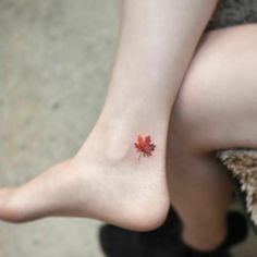 a small red leaf tattoo on the left side of her foot, which is sitting next to a woman's leg