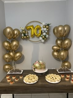 a table topped with cakes and desserts covered in gold foil balloons sitting on top of a wooden table