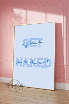 a white framed poster with the words get naked on it in blue ink against a pink wall