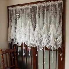 a window with sheer curtains hanging from it's side and a wooden chair in front of it