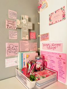 a white desk topped with lots of pink and purple items next to a wall covered in posters