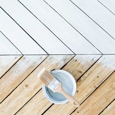 a paint can with a brush on top of it sitting on a wooden floor next to a white bucket