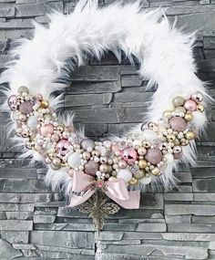 a wreath with white feathers, ornaments and pink bows on the front of a brick wall