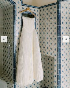 a white dress hanging on a blue and white tiled wall in a bathroom next to a toilet