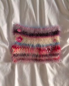 a close up of a knitted object on a white sheet with a pink button