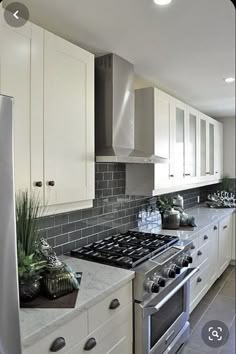 a kitchen with white cabinets and gray tile backsplash, stainless steel stove top