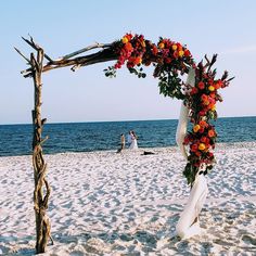 a wedding arch on the beach decorated with orange and red flowers for an outdoor ceremony