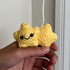 a hand holding two small yellow crocheted items with eyes and ears, one is smiling at the camera